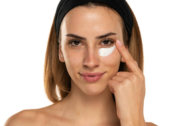 portret van een jonge vrouw aanbrengen cosmetische product onder haar ogen op een witte achtergrond - Foto, afbeelding