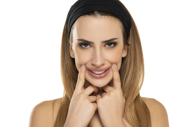 retrato de mujer joven estirando la boca con sonrisa falsa con los dedos sobre fondo blanco - Foto, Imagen