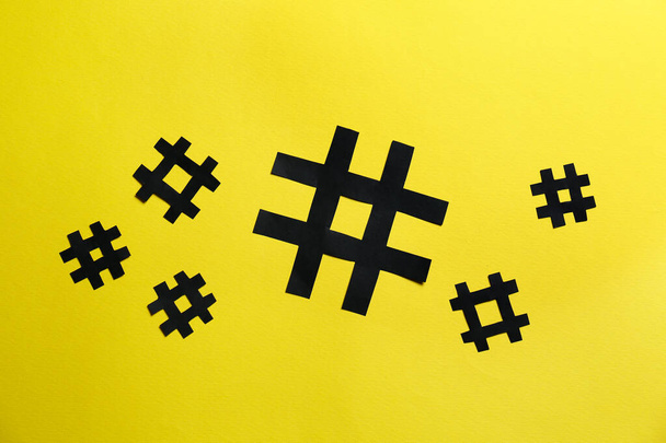 Black paper hashtag symbols on yellow background, flat lay - Foto, Imagen