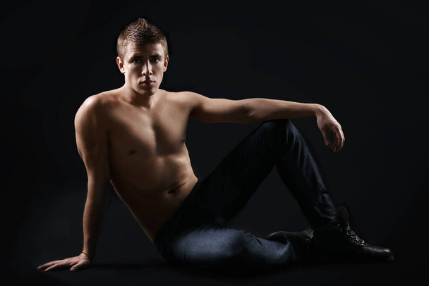 Sexy young man  in jeans sitting on the flor, back background, work in studio - Foto, immagini