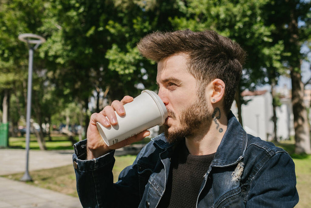 Young man wearing casual clothes drinking coffee. He is looking away while drinking coffee. - Photo, Image
