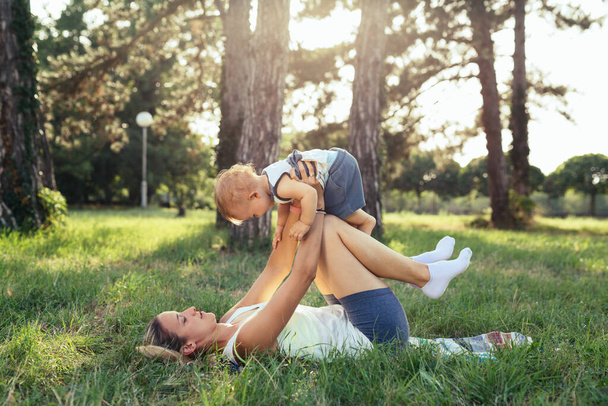 mother with her baby boy do physical exercises in public park - Photo, image