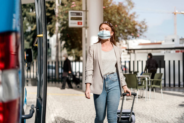 Mladá žena s ochrannou maskou nastupující do autobusu se zavazadly - Fotografie, Obrázek