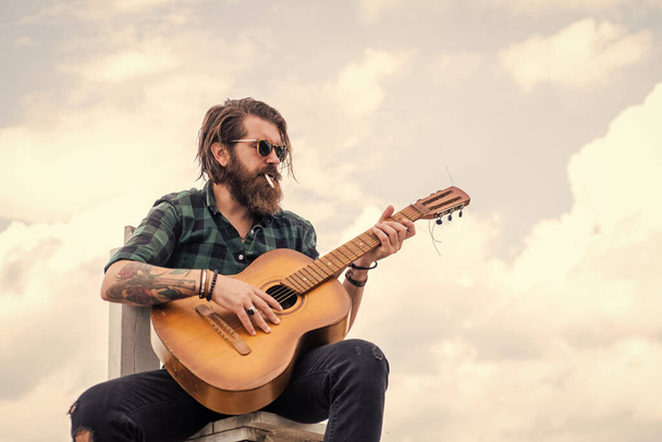 Sounds like music. hipster with long hair and moustache guitarist. male guitarist with musical instrument. country music concept. bearded man play acoustic guitar. casual guy express human emotions - Фото, зображення