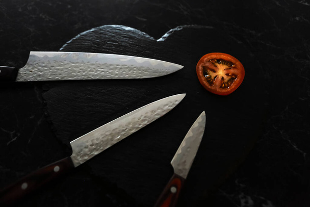 Coltelli e pomodoro tagliato sulla lavagna nera - Foto, immagini