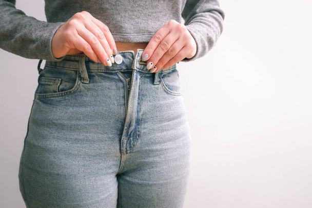 A woman in jeans and a top fastens a jeans button. Cropped shot of young woman buttoning up her jeans. - Foto, afbeelding