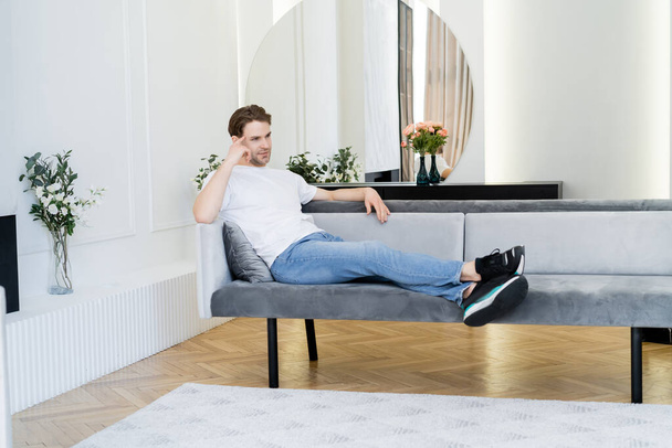full length view of dreamy man resting in living room decorated with flowers - Foto, Bild
