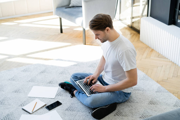 high angle view of man sitting on floor with crossed legs and typing on laptop - Valokuva, kuva
