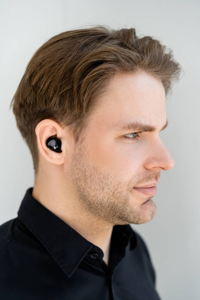 profile of young man listening music in wireless earphone isolated on grey - Valokuva, kuva