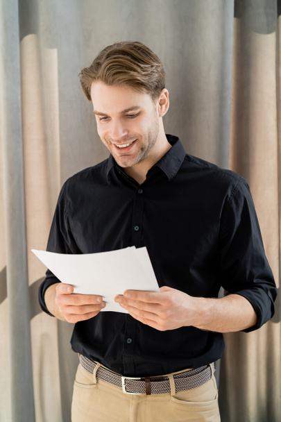 cheerful man in black shirt reading documents at home - Fotoğraf, Görsel