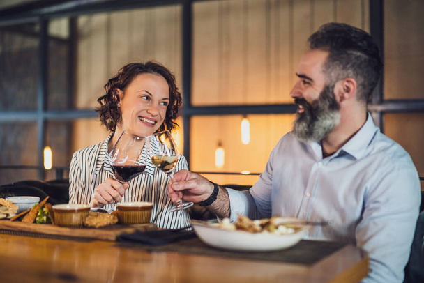Счастливая пара сидит в ресторане. Они ужинают с вином и хорошо проводят время вместе.. - Фото, изображение