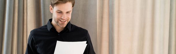 happy man in black shirt looking at documents near beige curtain, banner - Photo, Image