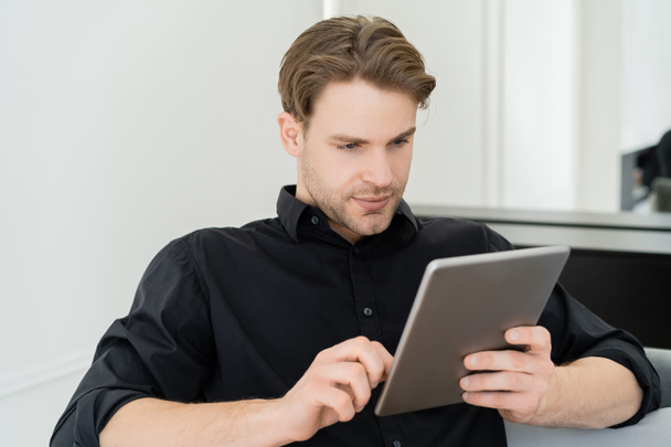 man in black shirt sitting at home and using digital tablet - Zdjęcie, obraz