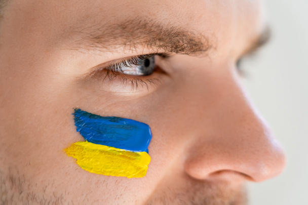 στενή άποψη του ανθρώπου με ουκρανική σημαία ζωγραφισμένη στο πρόσωπο απομονωμένη σε γκρι - Φωτογραφία, εικόνα