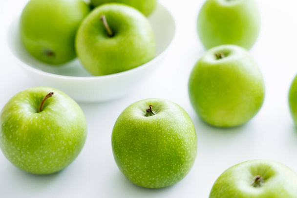 groene en rijpe appels in de buurt van kom op wit - Foto, afbeelding