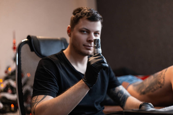 Hombre artista profesional del tatuaje con máquina de tatuaje preparándose para hacer un tatuaje en el estudio - Foto, Imagen