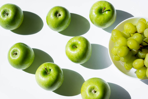 vista superior de maçãs maduras perto de uvas saborosas em tigela em branco - Foto, Imagem