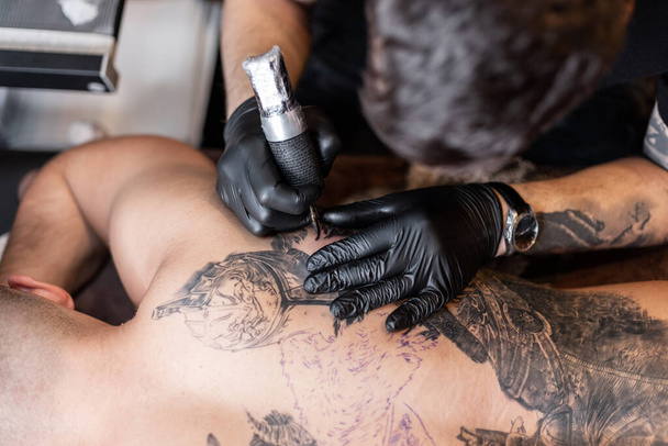 επαγγελματίας καλλιτέχνης τατουάζ εισάγει μαύρο μελάνι στο δέρμα χρησιμοποιώντας μια βελόνα από ένα μηχάνημα τατουάζ. - Φωτογραφία, εικόνα