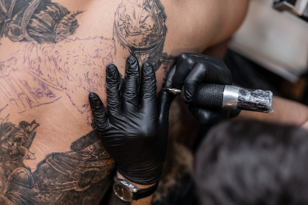 Dövme sanatçısı bir adamın vücudunda bir resim oluşturur. dövme makineleri ve elleri yakın çekim - Fotoğraf, Görsel