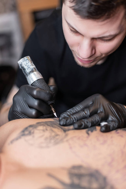 professional man tattoo artist stuffs tattoos, close-up. Modern tattoo machine in operation - Photo, Image