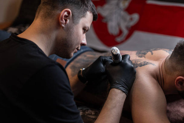 Tatuaje artista llena un tatuaje en la espalda de un hombre en el estudio - Foto, Imagen