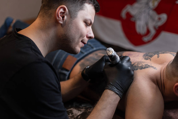 przycięte ujęcie tatuażysty w rękawiczkach pracujących nad tatuażem na ciele w salonie - Zdjęcie, obraz
