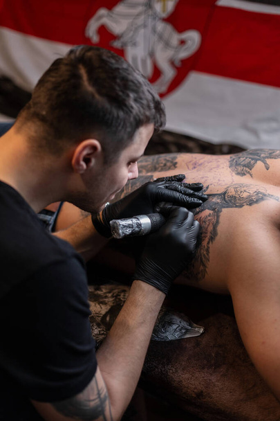 hombre tatuaje artista trabaja en un estudio y materias tatuaje en la espalda de un hombre - Foto, Imagen