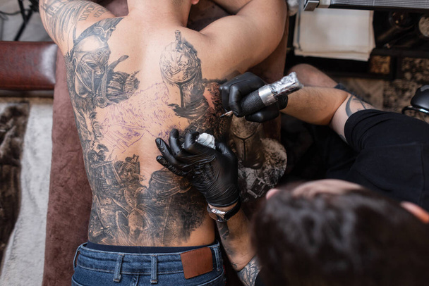 Szakmai férfi tetoválás mester egy tetováló gép rajzol egy lovag tetoválás egy férfi hátára, felső nézet - Fotó, kép