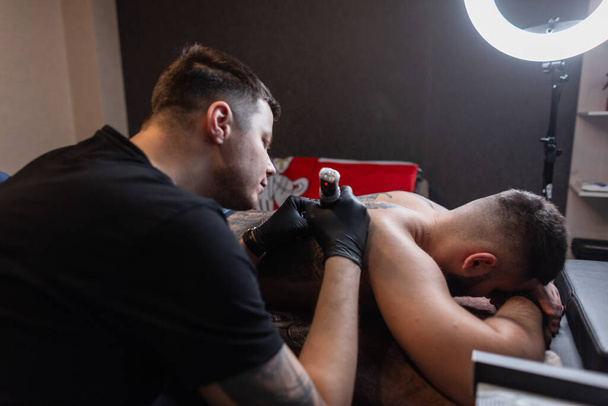 Hombre tatuaje maestro materias profesionales un tatuaje en la espalda de un hombre en el estudio, proceso de trabajo - Foto, Imagen