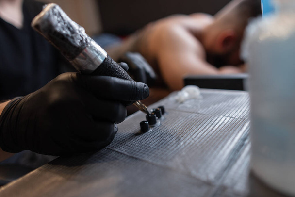 Человек татуировки мастер профессионал в черных перчатках с татуировкой машина собирая чернила, рабочий процесс. Мужская рука закрывается - Фото, изображение