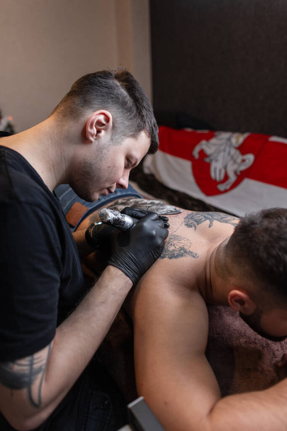 Dövme ustası evdeki adamın sırtına dövme yaptırıyor. - Fotoğraf, Görsel