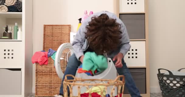Szczęśliwy causasian nastolatek rzucając brudne ubrania do pralki jako piłka. Yong chłopiec mając zabawy rzucając ubrania do pralki w pralni. - Materiał filmowy, wideo