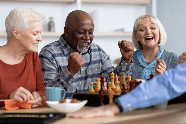Emotional black man playing chess with multiracial friends - Photo, Image