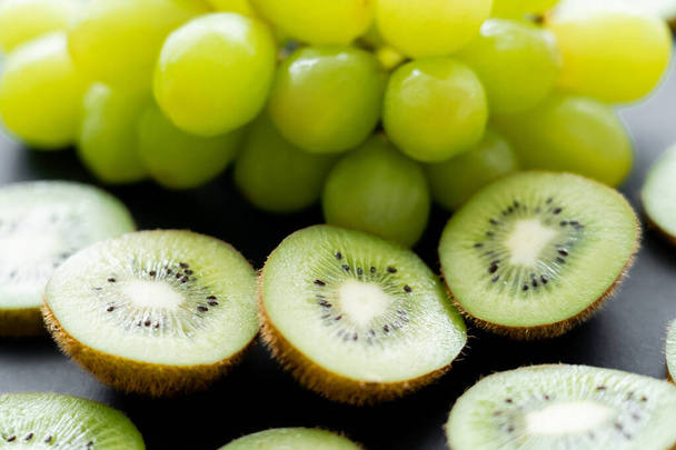 close up view of green grapes and sliced fresh kiwi on black  - Foto, Bild