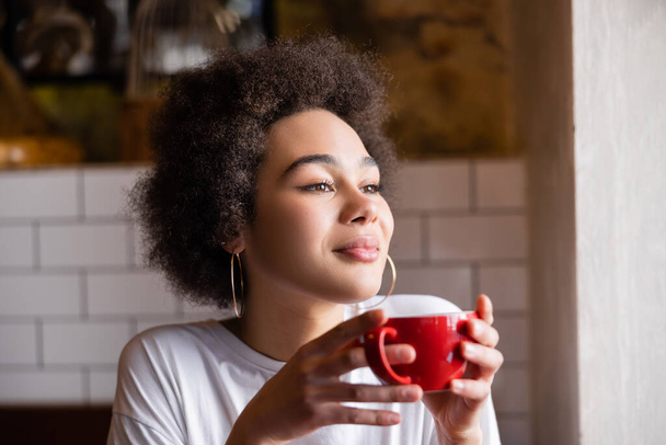 curly african american woman in hoop earrings holding cup of coffee  - Foto, Imagem