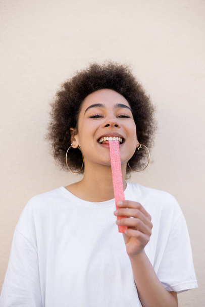 happy african american young woman eating sweet jelly strip on white - Photo, image