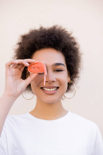 feliz africano americano joven mujer celebración jalea burbuja cinta cerca ojo en blanco - Foto, imagen