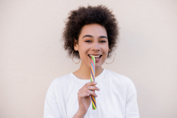 šťastný africký americký mladý žena v obruč náušnice jíst želé pruh na bílém - Fotografie, Obrázek