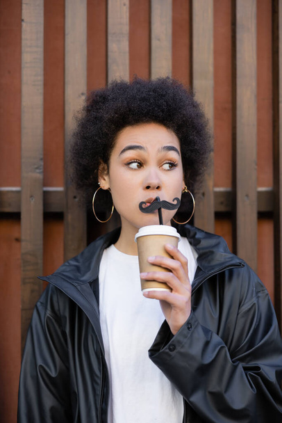νεαρή Αφροαμερικανή που κρατάει χάρτινο κύπελλο και καλαμάκι με μουστάκι - Φωτογραφία, εικόνα