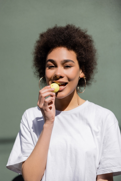 joyful african american woman eating yellow candy  - 写真・画像