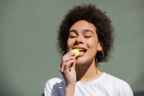pleased african american woman eating yellow candy  - Foto, Imagen