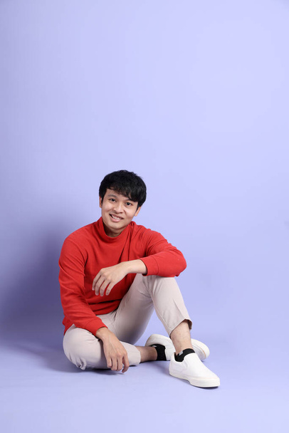 The young adult southeast Asian man with red long sleeve shirt sitting on the purple background. - Fotoğraf, Görsel