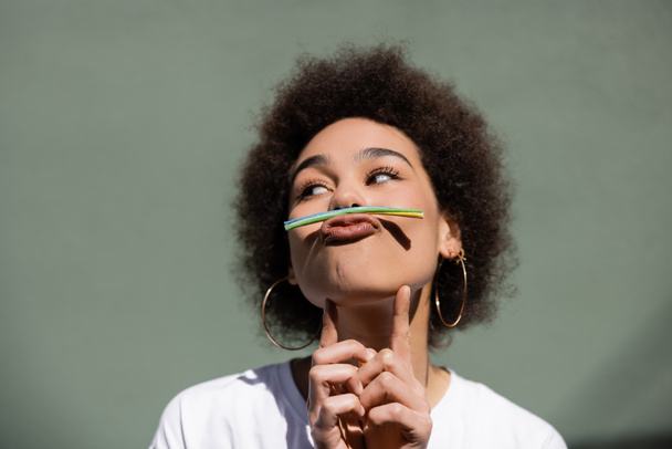 νεαρή Αφροαμερικανή που κρατάει άχυρο ζελέ με το στόμα ενώ γρυλίζει έξω - Φωτογραφία, εικόνα