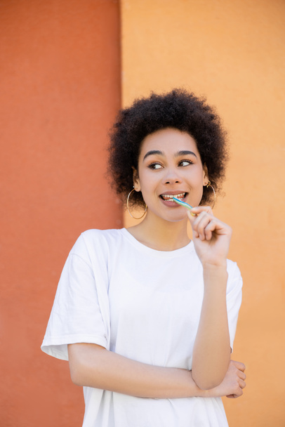 радісна афроамериканська жінка їсть смачну желеву соломинку біля помаранчевої стіни
 - Фото, зображення