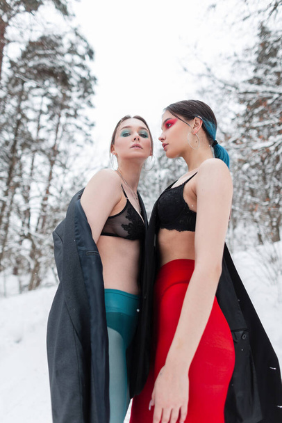 Dvě krásné sexy ženy s make-upem v módním oblečení s podprsenkou, punčocháči a stylovými sako v zimním lese se sněhem. Vogue ženský styl a krása - Fotografie, Obrázek