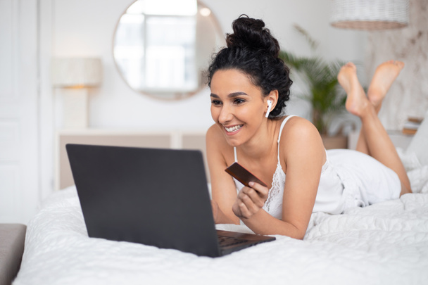 Happy pretty millennial europese brunette dame met draadloze hoofdtelefoon doen online winkelen in laptop - Foto, afbeelding