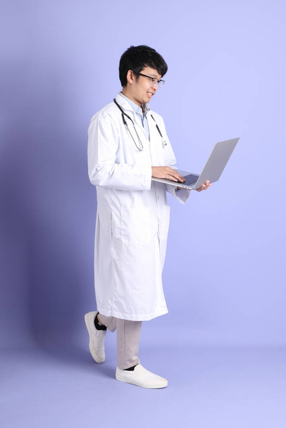 The young adult Asian physician standing on the purple background. - Фото, зображення