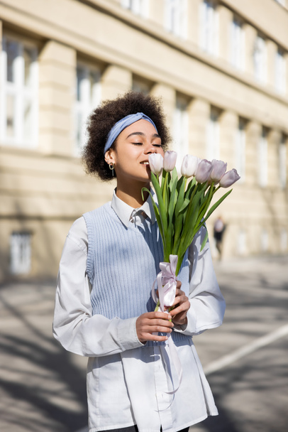 joyful african american woman looking at tulips on street  - 写真・画像