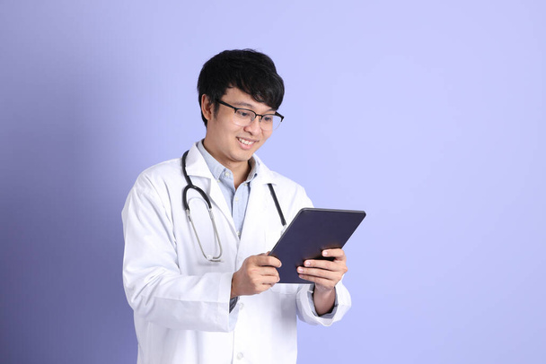 The young adult Asian physician standing on the purple background. - Foto, afbeelding