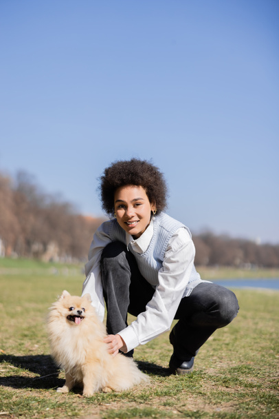happy african american woman cuddling pomeranian dog in park - Photo, image